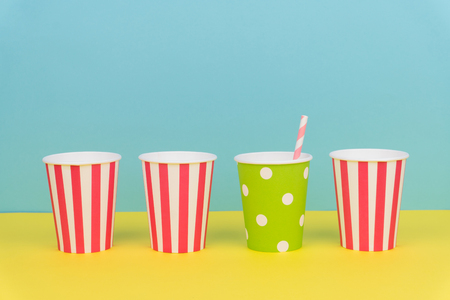 colorful party paper cups and striped straw on yellow table with blue backgroundの写真素材