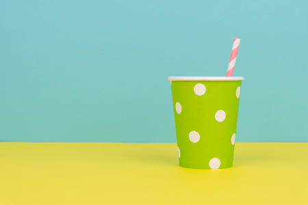 a green polka dot party paper cup with pink striped straw on the yellow table with blue backgroundの写真素材