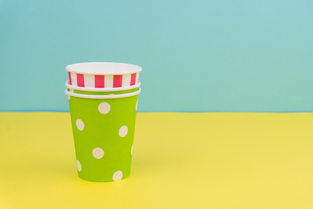 stack of colorful party paper cups on yellow table with blue backgroundの写真素材