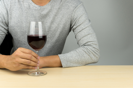 man in grey shirt with a glass of red wine at the wooden tableの写真素材