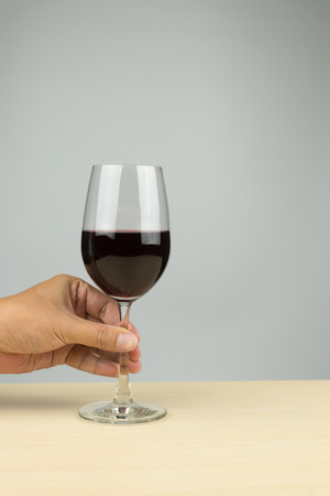 hand putting a glass of red wine on the wooden tableの写真素材