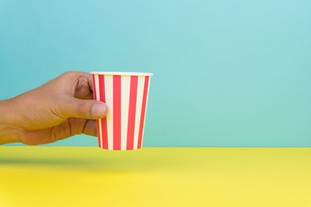 hand holding a colorful party paper cup, yellow and blue backgroundの写真素材