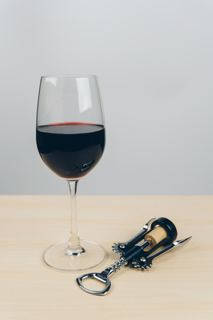 a glass of red wine and a metal corkscrew with attached cork on the wooden tableの写真素材