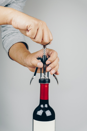 man in grey shirt opening a red wine bottle with a metal corkscrewの写真素材