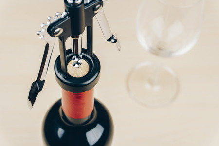opening a red wine bottle with a corkscrew, empty wine glass on the wooden tableの写真素材