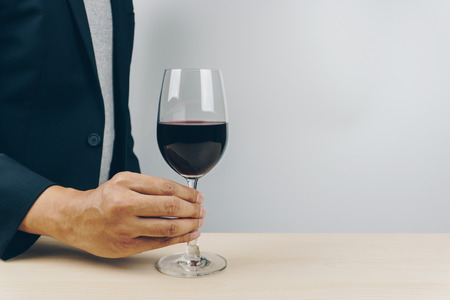 man in grey shirt and black suit putting a glass of red wine on the wooden tableの写真素材