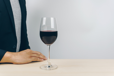 a glass of red wine on the wooden table, man in grey shirt and black suit in the backgroundの写真素材