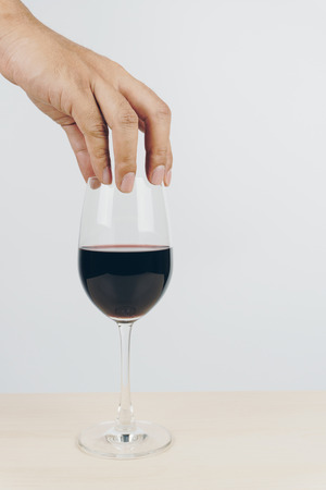 hand putting a glass of red wine on the wooden tableの写真素材