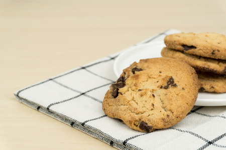 the chocolate chip cookies in a white round dish on the cloth at the wooden table.の写真素材