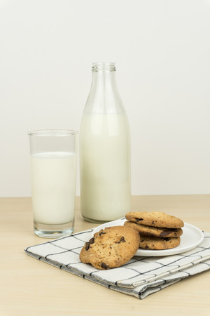 a glass of milk with milk bottle and the chocolate chip cookies in a white round dish on the wooden table.の写真素材