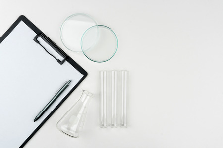 top view of laboratory equipments. A clipboard with pen, flask, test tubes and Petri dish on the tableの写真素材