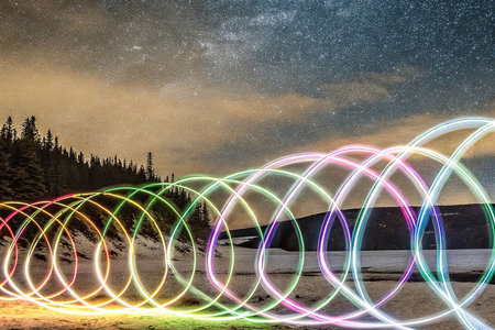 Night light trails spiral on sandy beach under starry skyの素材