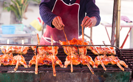 Asian man is grilling chickens on the grillの写真素材