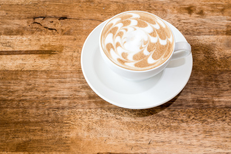 A cup of coffee with flower pattern in a white cup on wooden backgroundの写真素材