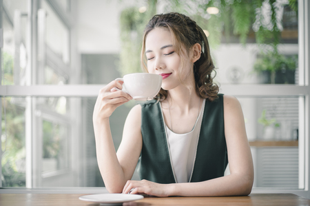 Portrait of Asian woman smiling in coffee shop cafe. Beautiful girl with coffee cup in the morning.の写真素材