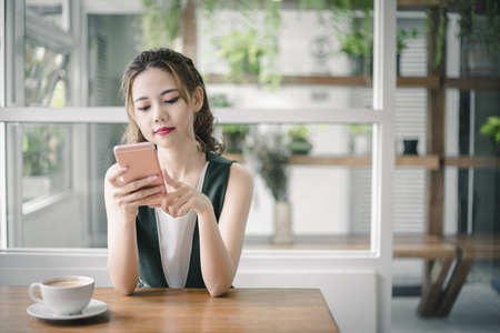 Young beautiful Asain lady touching and browsing her smart phone at home.の写真素材