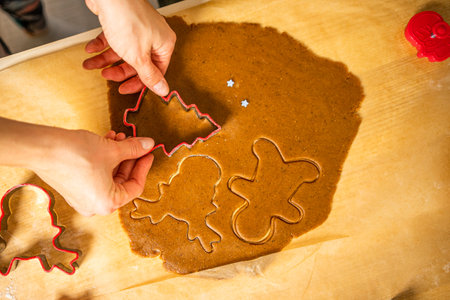 Cutting of gingerbread shapes. A young woman cuts gingerbread shapes on bruna baking paper. Red gingerbread shapes.の写真素材