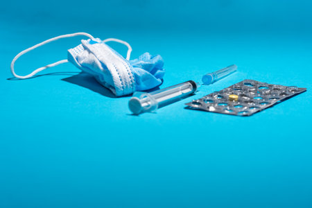 Blue face mask, pills, syringe on blue background. Medicine and healthcare. Medications and pharmacy. Low prespective.の写真素材