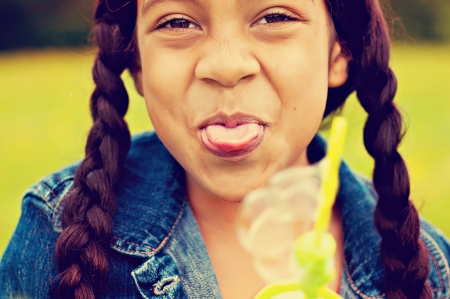 Young girl sticking tongue out with bubbles in handの写真素材