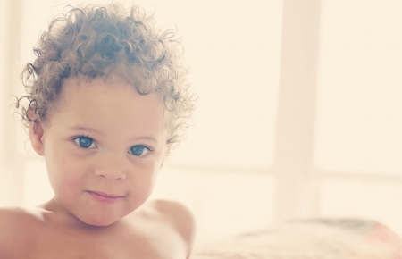 Precious little boy sitting on bed smilingの写真素材