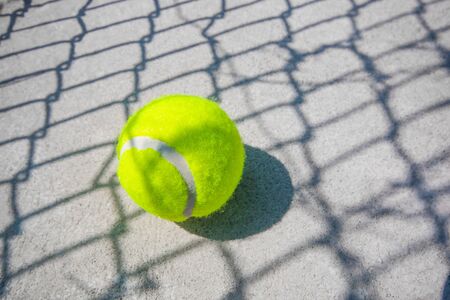 The tennis ball is placed on the concrete floor. There is a shadow of the net.の写真素材