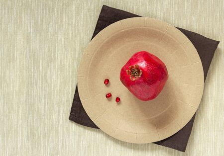 Healthy, immune-boosting seasonal fruits. A ripe, juicy pomegranate lying separately on a craft disposable plate on a brown napkin. Food photo, copy space, horizontal orientationの写真素材