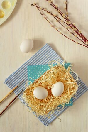 Fresh, raw, white eggs on straw on a wooden background with brushes, palette and willow twigsの写真素材
