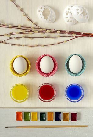 Preparing for the celebration of Easter, spring mood. Whole, raw white eggs prepared for coloring and decorating with blue, red, yellow paints. watercolor, brush and willow branches. A cozy home is a pleasant pastimeの写真素材