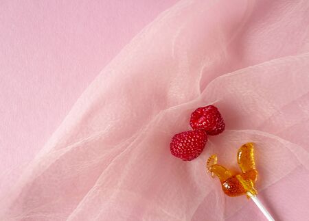 Two whole ripe raspberries with a Lollipop on a pink veil backgroundの写真素材