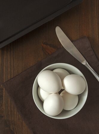 The concept of a simple healthy natural food. Chicken, white, fresh farm eggs in a white bowl prepared to cook an omelet on a dark wooden background. Food photo, vertical orientationの写真素材