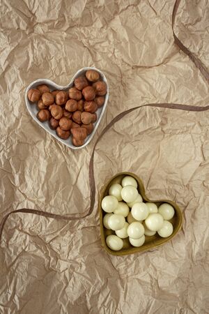 Concept of food designed for Valentine's day. Raw nuts and hazelnuts in white chocolate in gift molds in the form of hearts. Healthy eating in eco-friendly packaging. Food photo, top view, vertical orientationの写真素材