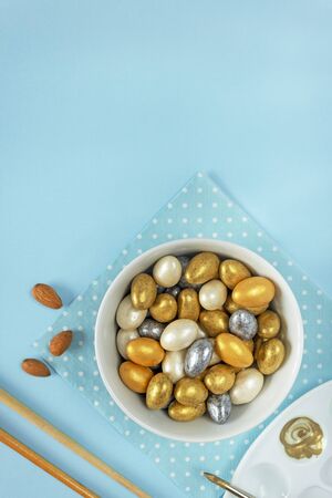 Almonds in yellow, silver, gold and white glaze lie in a bowl on a blue backgroundの写真素材