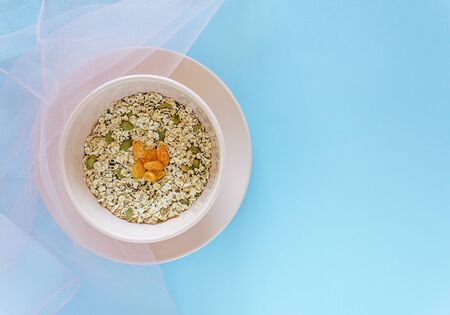 Pink bowls with oatmeal, raisins, nuts and seeds on a blue backgroundの写真素材