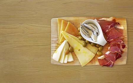 Croatian traditional food, Dalmatian plate. Proshut, cheese sprinkled with olive oil with capers in a pickle with olives on a wooden dish on a background with a copy space.The perfect appetizer for wineの写真素材