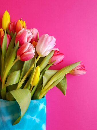 Spring holiday bouquet for Women's Day. Flowers in eco-friendly textile packaging. Concept without plastic. Multi-colored tulips in a woven bag on a pink background. Vertical orientationの写真素材