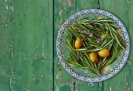 Green olives in bowl with rosemary sprigs on an old green board tableの写真素材