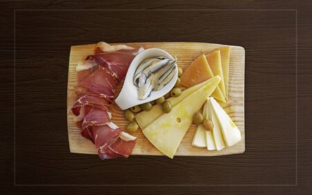 Croatian traditional food, Dalmatian plate. Proshut, cheese sprinkled with olive oil with capers in a pickle with olives on a wooden dish on a background with a copy space and frame.The perfect appetizer for wineの写真素材