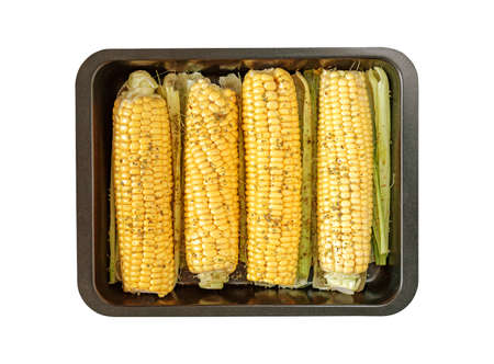 Isolated black baking tray with corn cobs with spiced, leaves on a white backgroundの写真素材