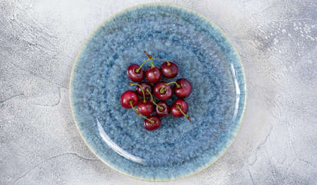 Fresh, ripe, sweet cherry on textural, beautiful plate on blue background. Concept of beauty of natural, ecological, seasonal berries and fruits. Food photo, horizontal orientationの写真素材