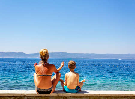 Grandmother and grandson sit in the lotus position and meditate on the beachの写真素材