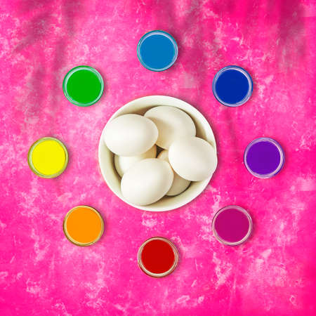 Whole, fresh, raw, white eggs in a white bowl with jars of rainbow paint on a bright pink background with the shadow of palm leaves. Festive, sunny mood in preparation for Easter, Palm Sundayの写真素材
