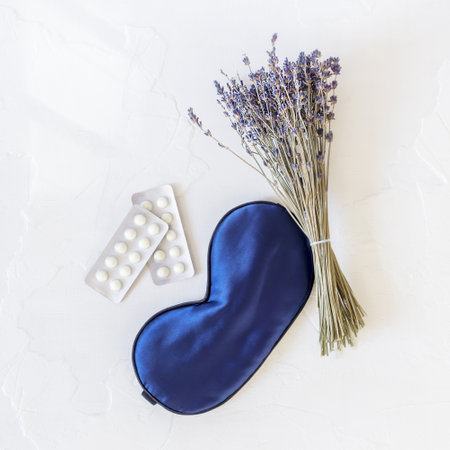 Flat lay composition with lavender flowers, mask for sleep and sleeping pills at once on a white background. Insomnia or depression treatment for sleepless nights. Sleep care is the new selfcareの写真素材