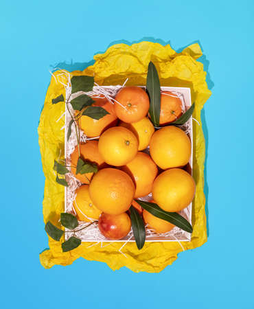 Fresh orange with leaves in a white box on a blue background. Healthy season foods with lots of vitamins. Foods rich in vitamin C. Eco friendly fruits packaging and storage. Vertical banner, top viewの写真素材