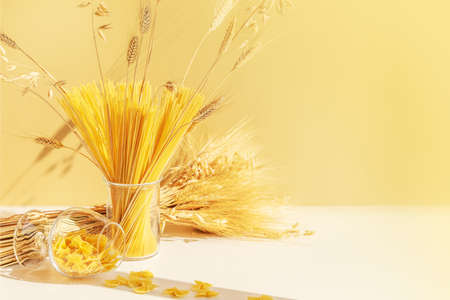 Food composition of raw spaghetti, farfalle pasta in a glasses with a bouquet of wheat on a white table with copy space. Zero waste concept, no plastic. Eco friendly sale and storage of bulk productsの写真素材