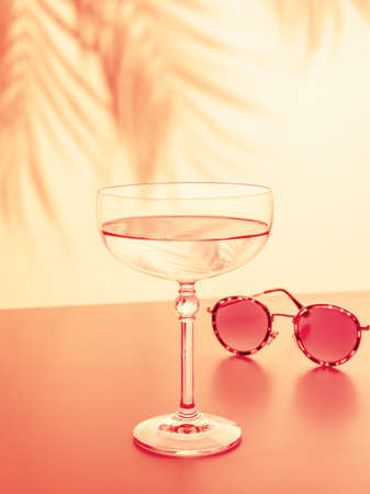 The concept of a tropical holiday resort and relax. Drink composition with a glass of rose wine and sunglasses on the background of the sunset with palm leaves shadows. Summer party. Selective focusの写真素材