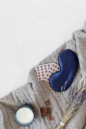 Vertical composition with comfortable, knitted blanket with a mask for sleep, pills, a bouquet of lavender, a glass of milk and sweet snack for good sleep. Men insomnia or depression treatmentの写真素材