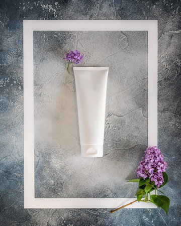 White plastic cosmetic tube in a white frame with a sprig of lilac on a blue background