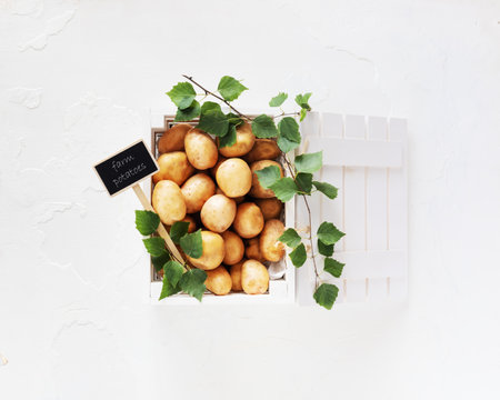 New crop, natural, farm potatoes in a white wooden box with the inscription farm potatoes and leaves on a white background. Selling seasonal vegetables at the local market. Flat layの写真素材