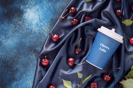 Food composition with craft cup of coffee, cherries and leaves on a blue, satin, folded background...