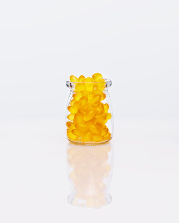 Yellow, gelatin capsules in a glass bottle on a white table with reflection